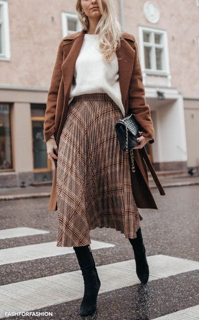 Camel coat worn over a brown plaid pleated midi skirt
