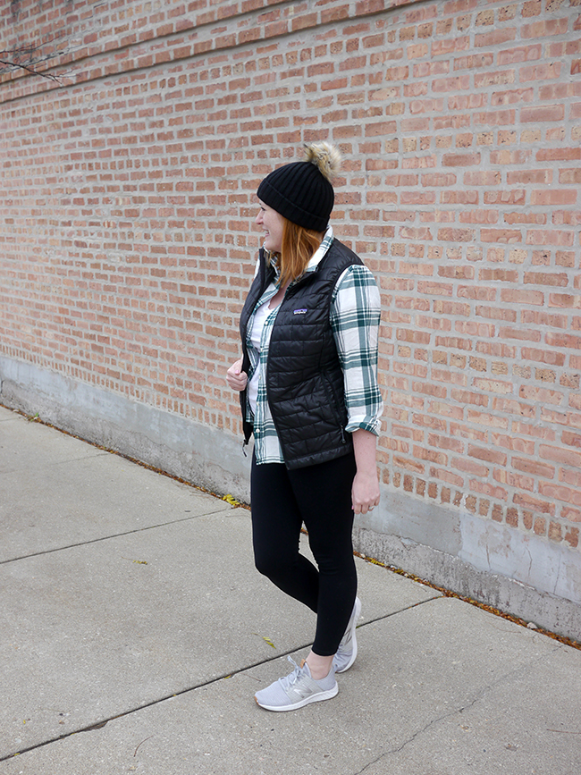 Woman wearing a quilted vest over a flannel shirt with a beanie
