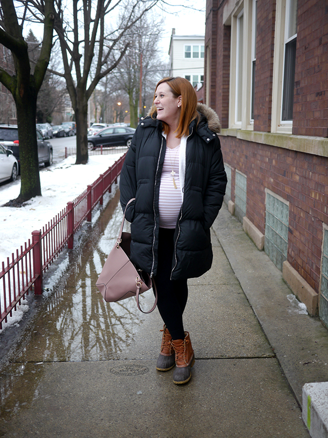 Woman in a black puffer, striped top and black leggings with tan duck boots on a wet sidewalk
