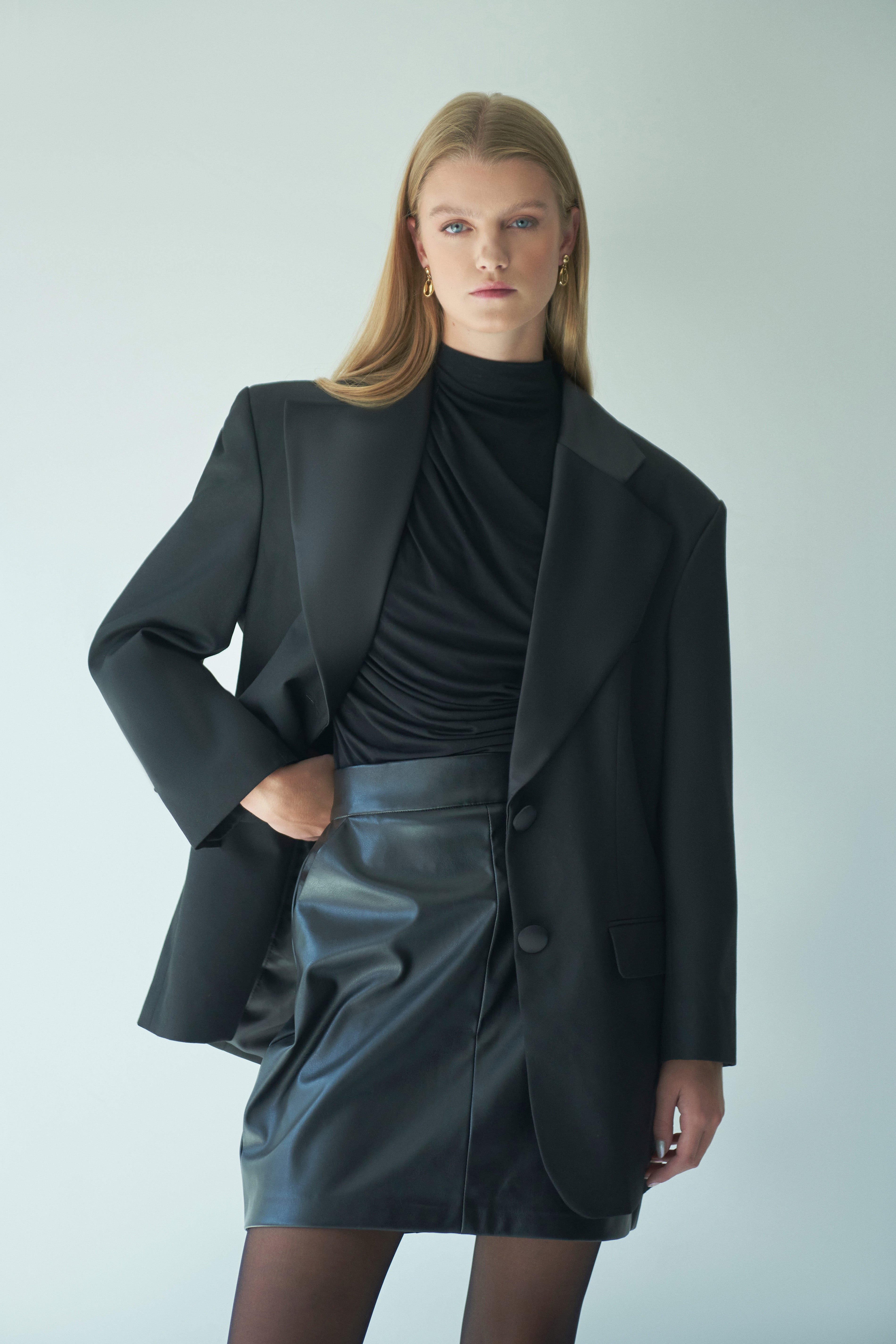 Model in black leather mini skirt with oversized black blazer and turtleneck