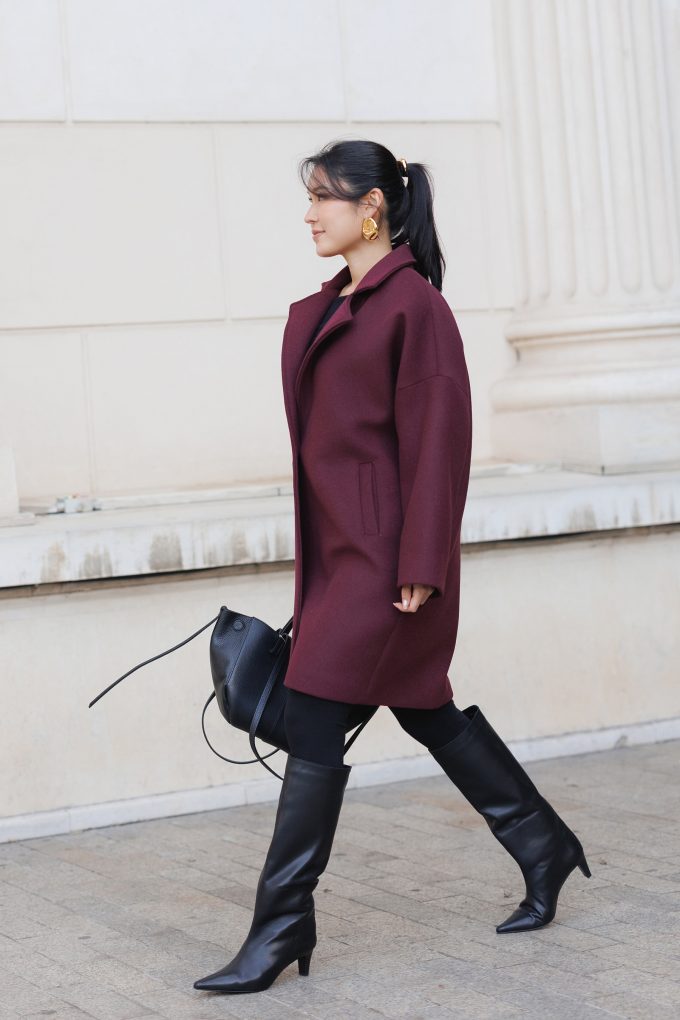 Woman in a burgundy oversized wool coat with black leggings and black knee-high heeled boots