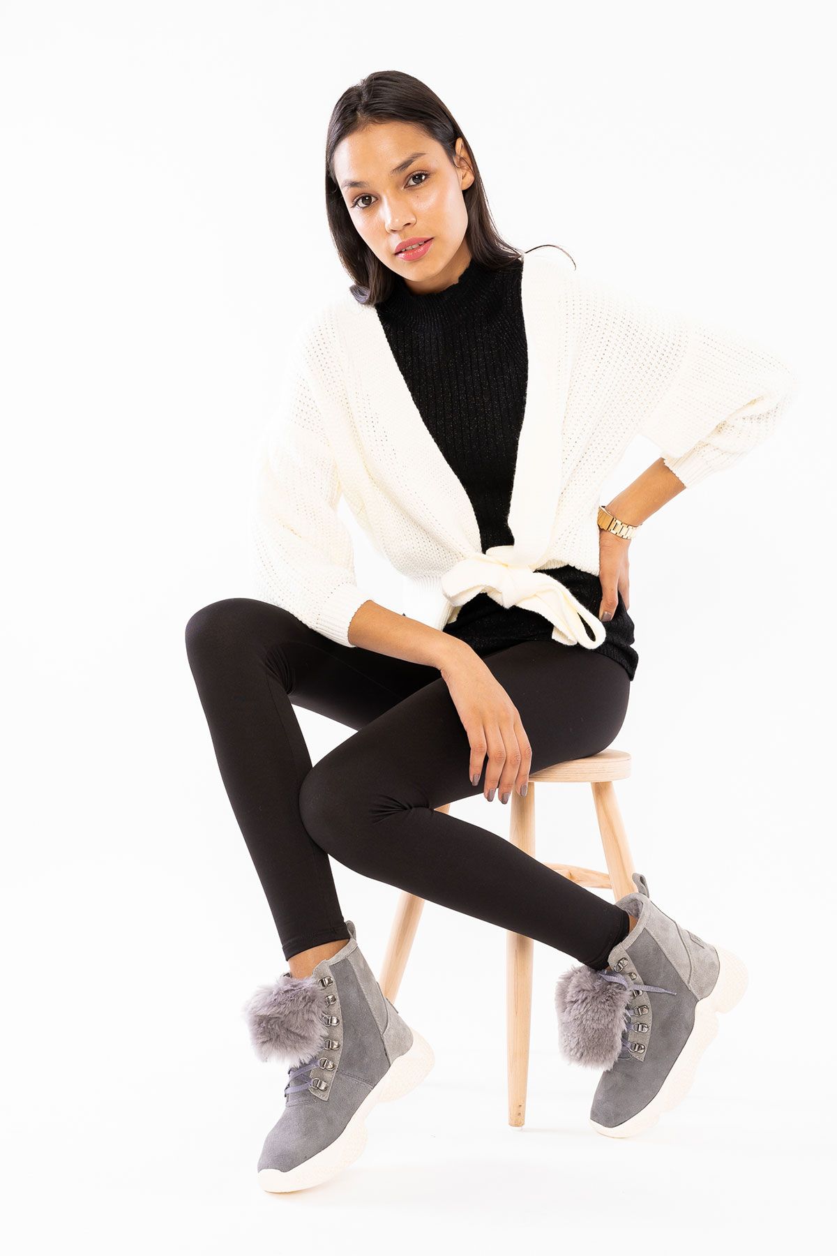 Woman in a cream chunky knit cardigan with leggings and boots