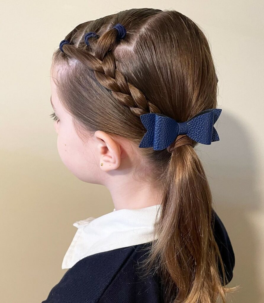 Little girl with side braids pulled into a low ponytail with a navy bow