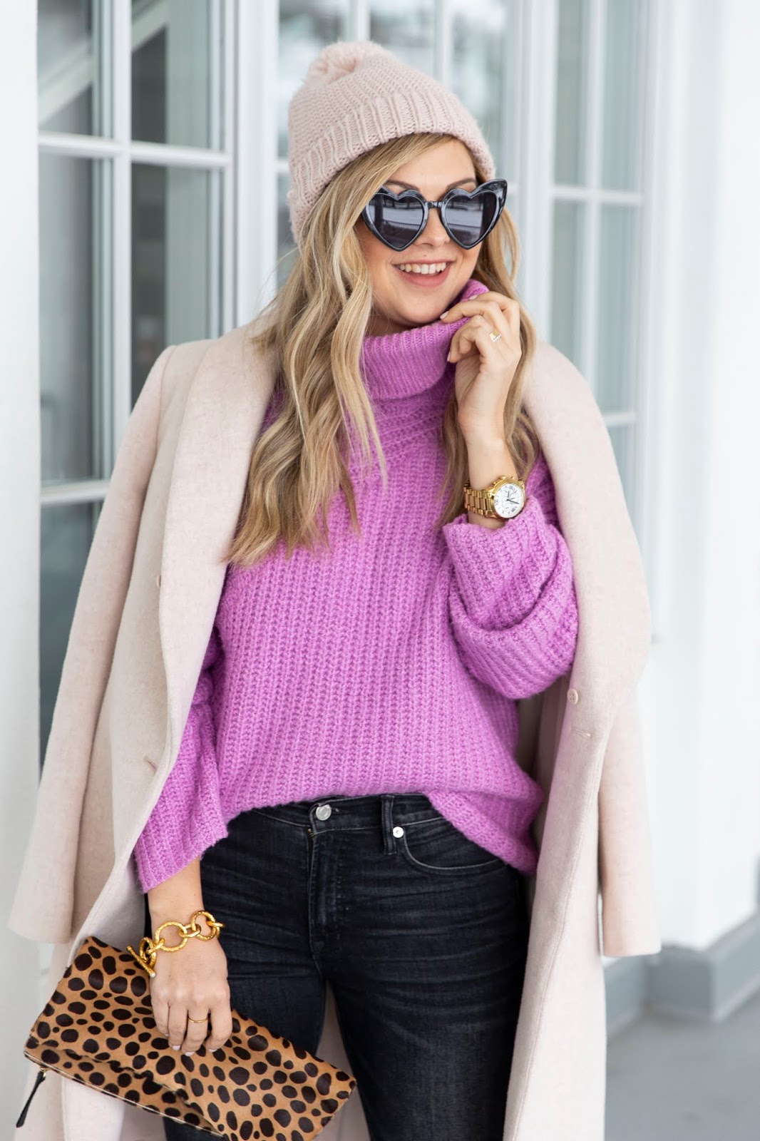 Woman in a blush beanie, pink turtleneck, heart sunglasses and leopard clutch