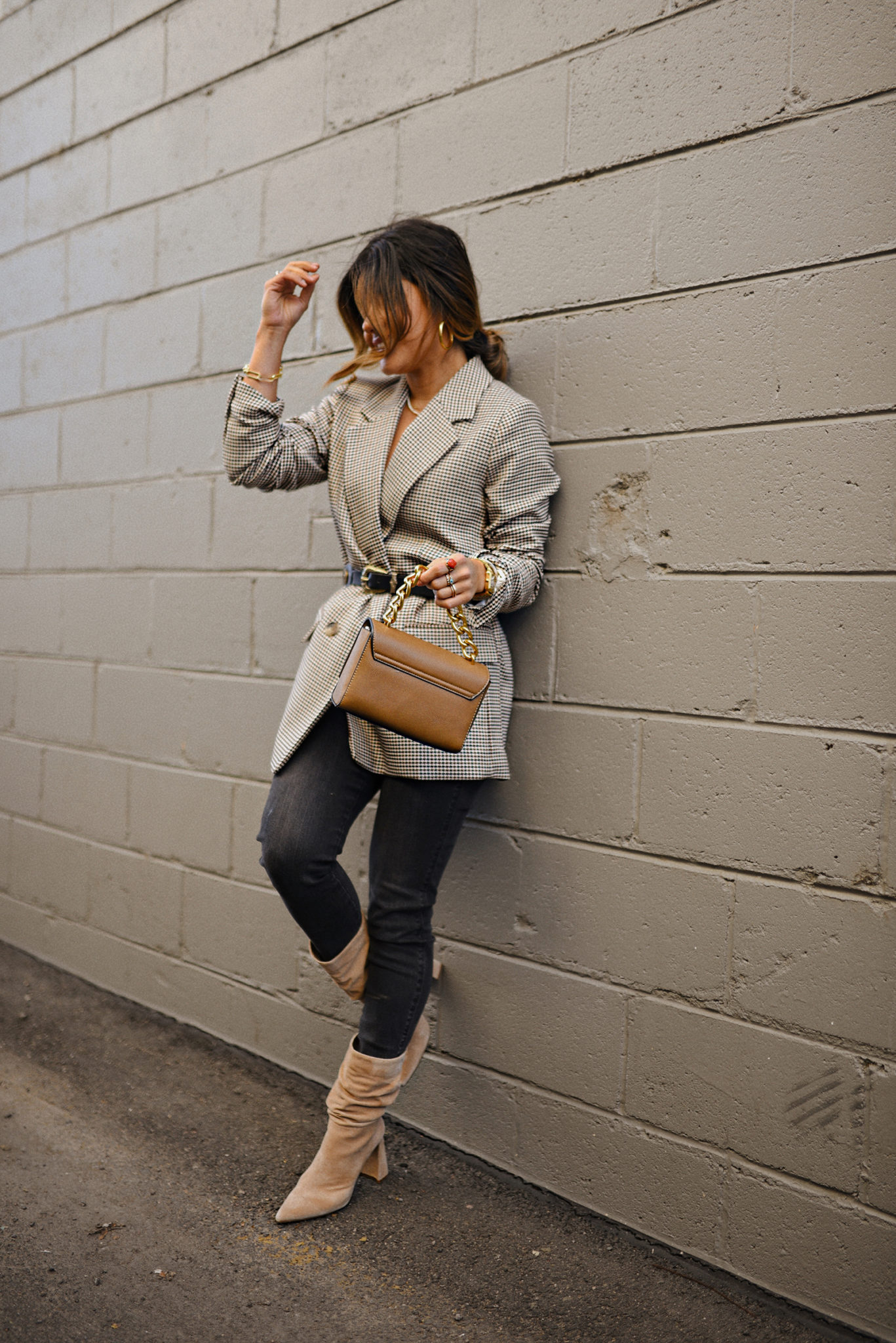 Woman wearing tan suede slouchy ankle boots with a houndstooth blazer, black skinny jeans and a tan handbag