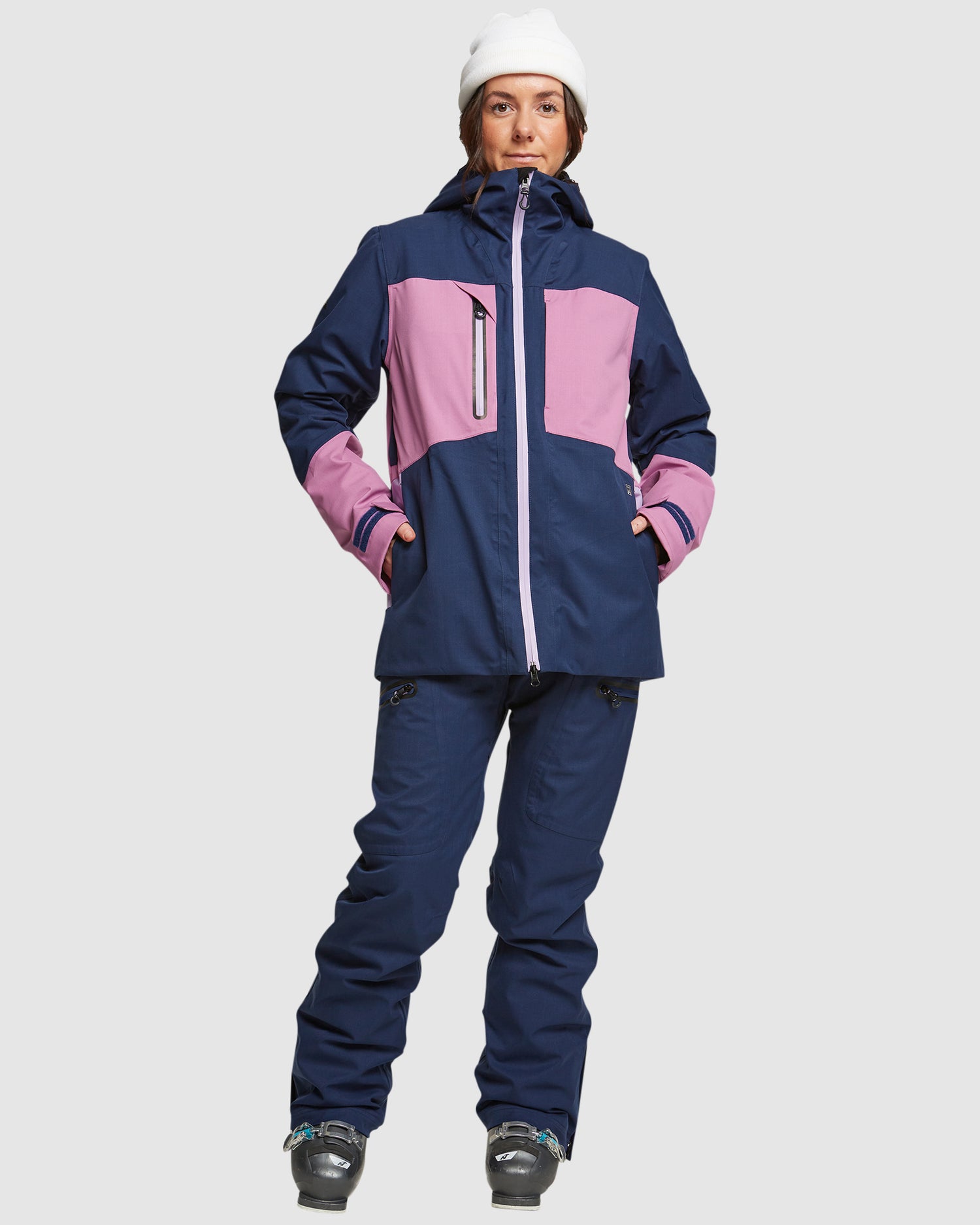 Woman wearing a navy and pink color-block ski jacket with navy ski pants and a white beanie