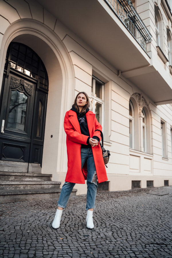 Woman wearing a long red winter coat with dark layers and boots