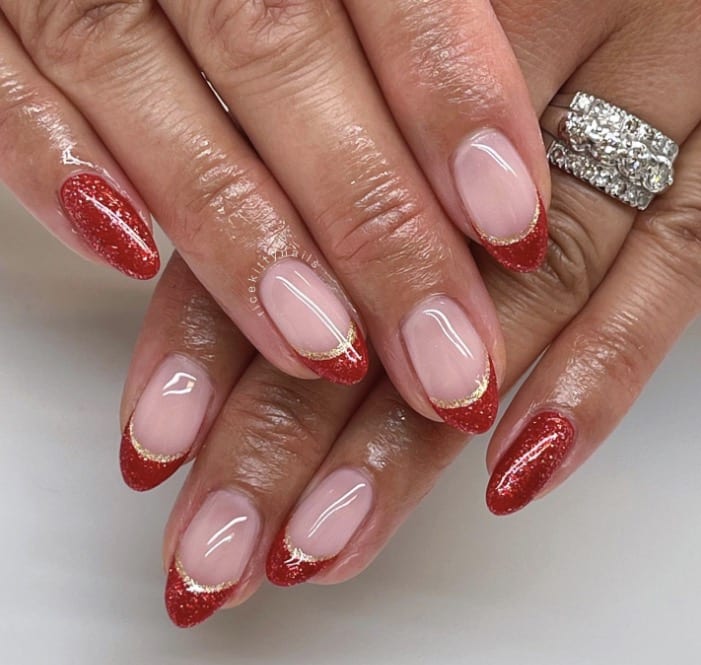 Almond nude nails with red glitter French tips and fine gold lines at the smile line