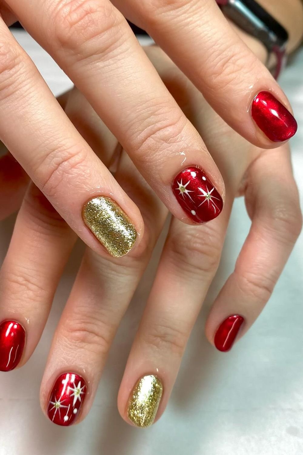 Short oval metallic cherry red nails with starburst art and gold glitter accent nails