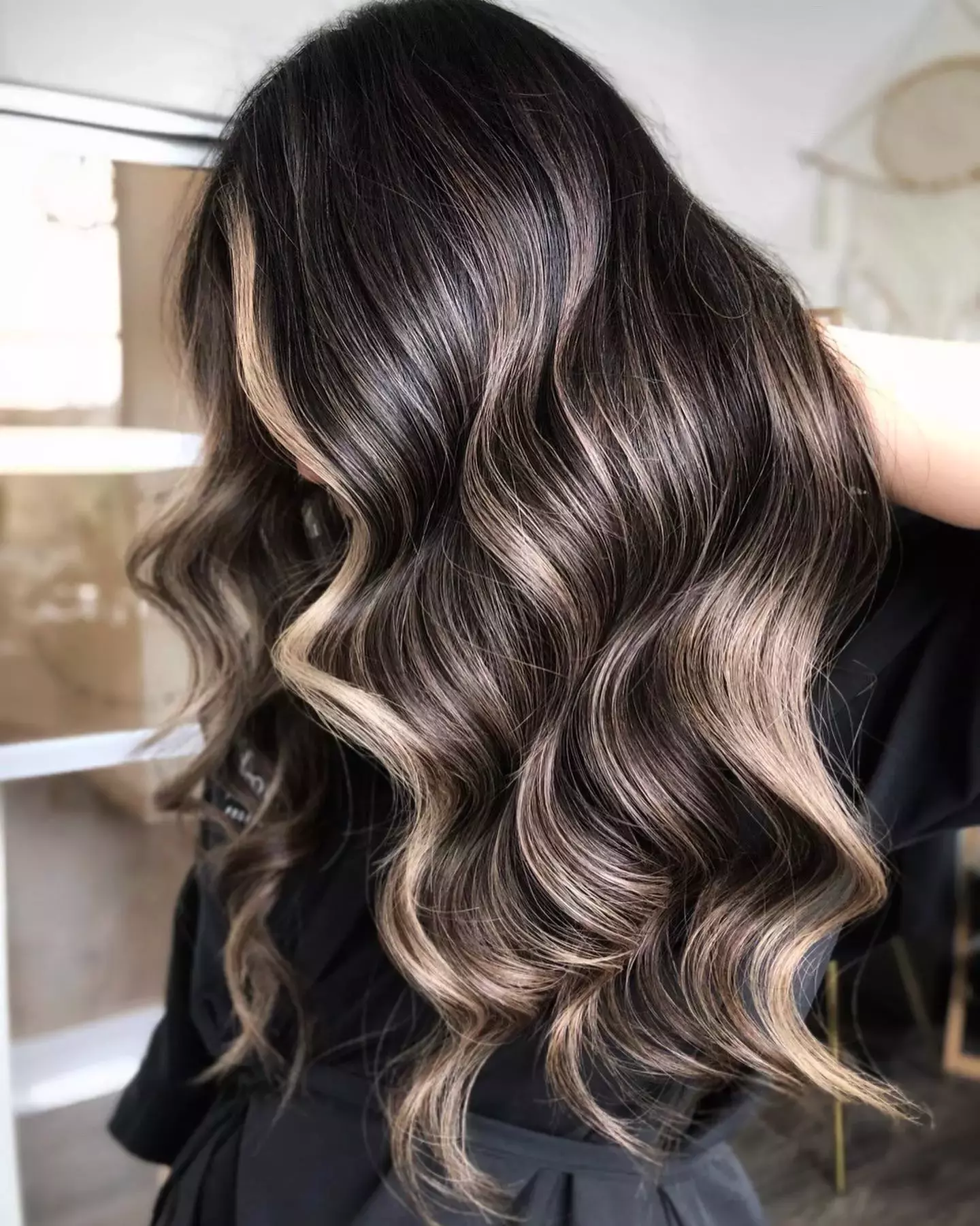 Back view of long wavy hair with dark espresso roots melting into golden-blonde balayage ends