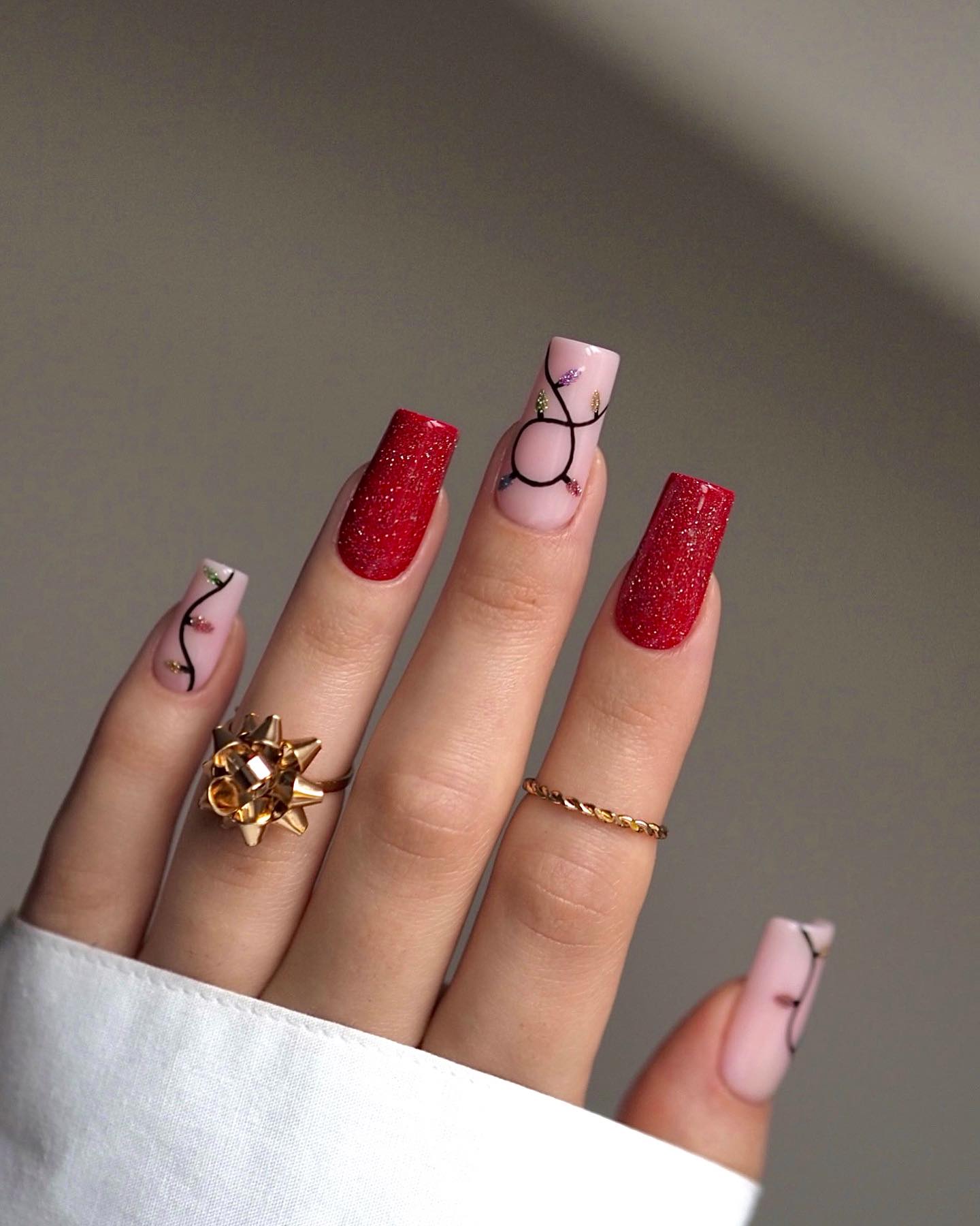 Ruby red glitter nails with nude accent nails featuring painted Christmas string lights