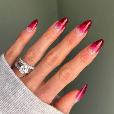 Ruby red glitter ombre stiletto nails, close-up on a hand in a grey sweater sleeve