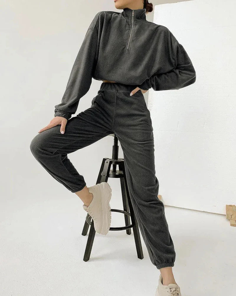 Woman wearing a dark gray half-zip fleece pullover with matching joggers and chunky white sneakers