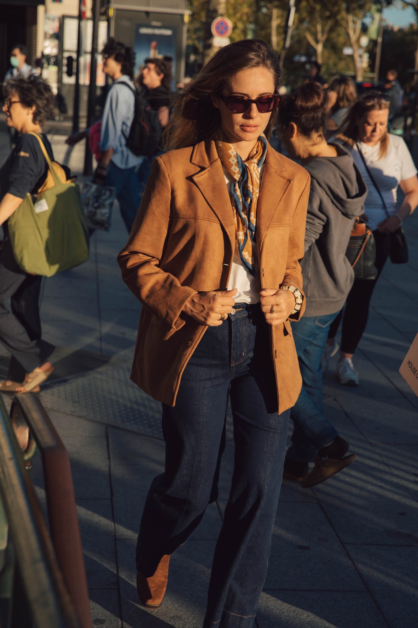 Woman in cognac suede ankle boots with a camel suede blazer, white shirt, silk scarf and dark jeans