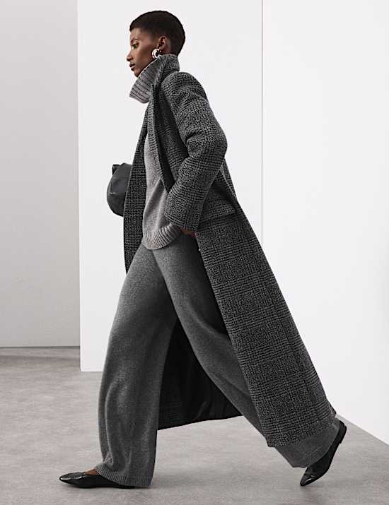 Woman in a charcoal textured long coat with a grey turtleneck and grey wide-leg trousers