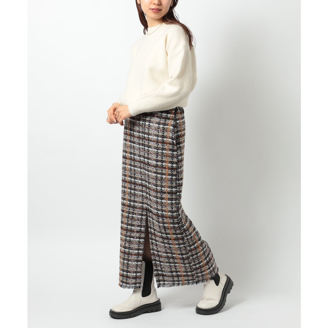 Woman in a cream sweater and long tweed plaid skirt with white Chelsea boots