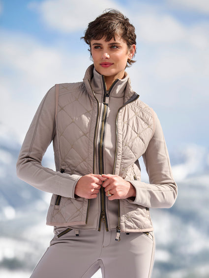 Woman in a beige quilted vest over a matching cashmere set on a snowy mountain