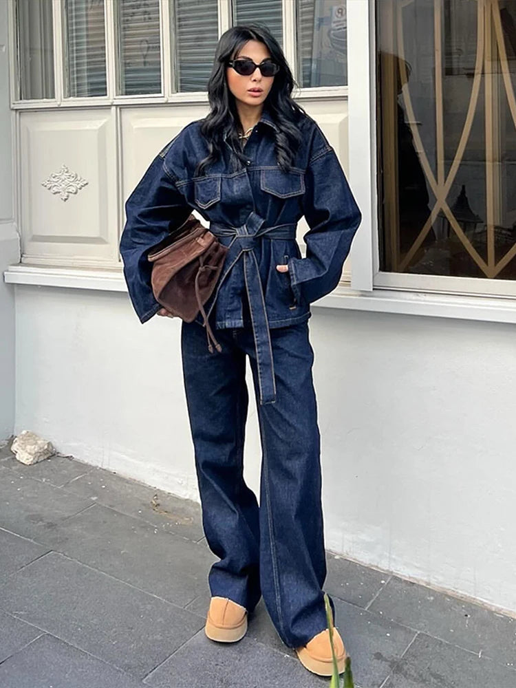 Woman in a belted dark denim shirt-jacket with dark wide-leg jeans, tan platforms and a brown bag