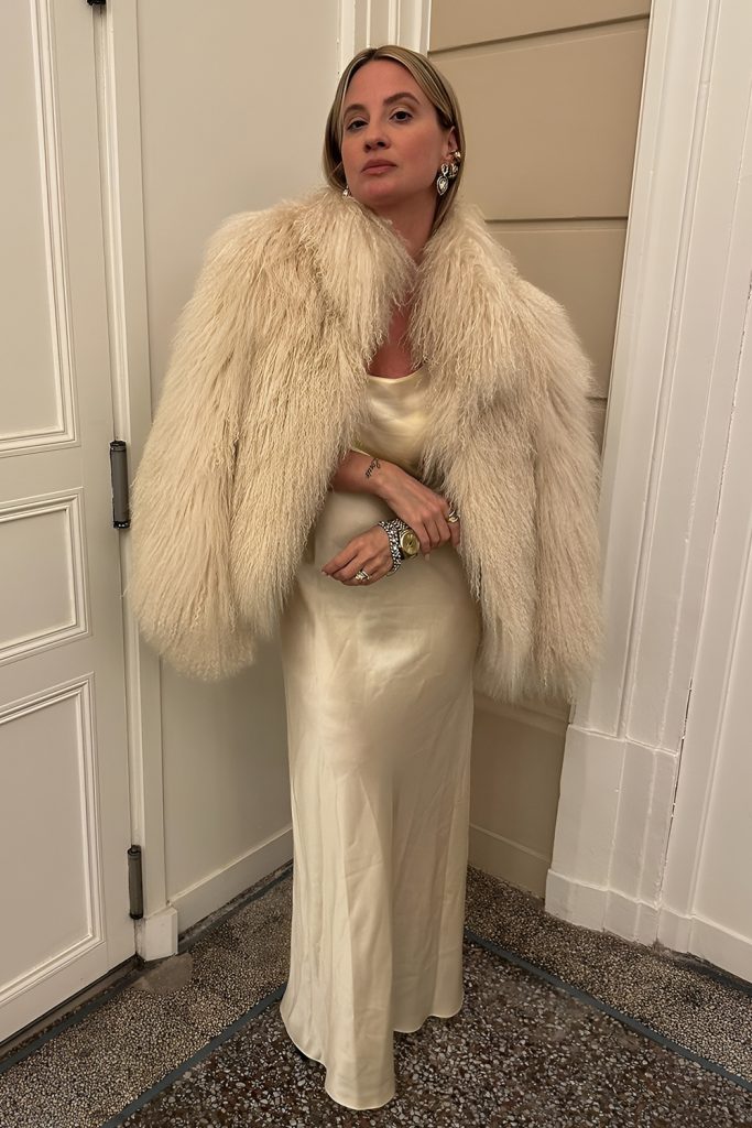 Woman wearing a cream satin slip dress with a shaggy cream faux fur coat and statement earrings