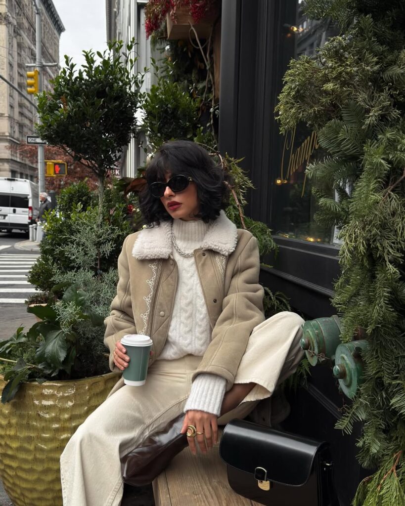 Tan shearling-collar jacket with a cream cable turtleneck, cream wide-leg trousers and a black bag