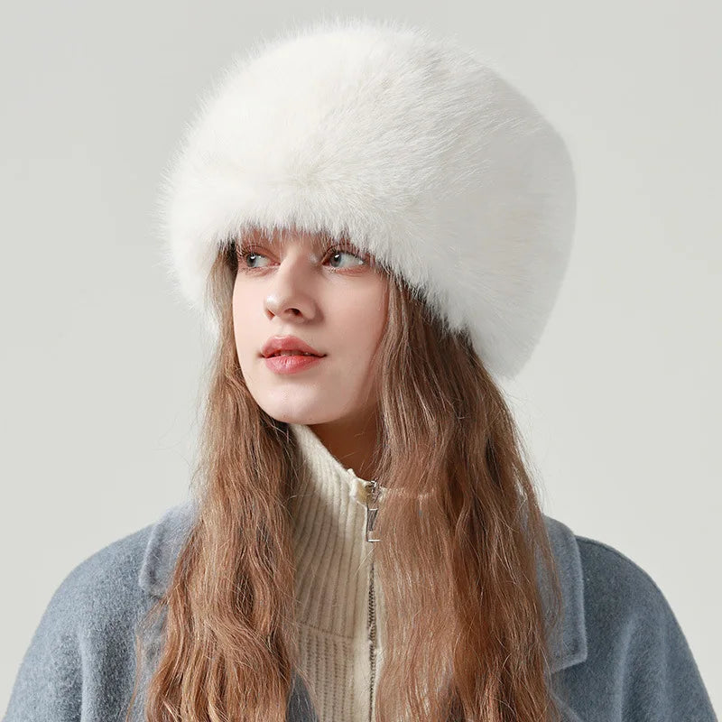 Model wearing a white faux fur hat with a cream knit and grey coat, studio portrait