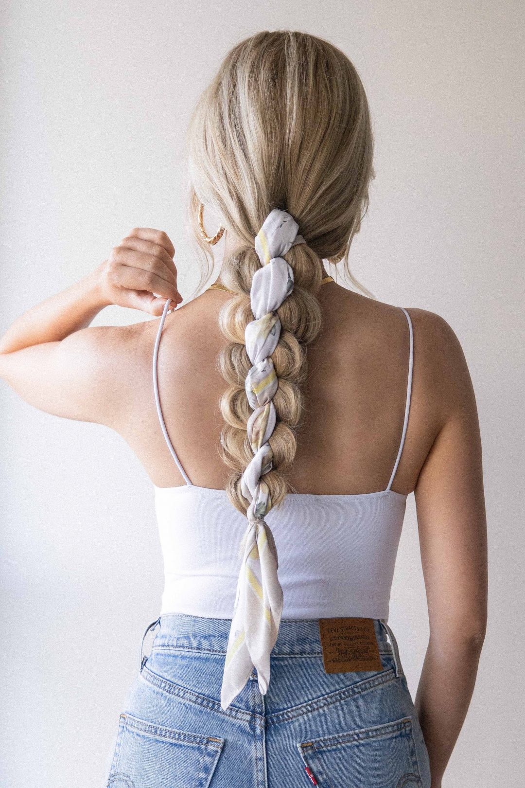 Long braided ponytail with a white and yellow scarf woven through the braid