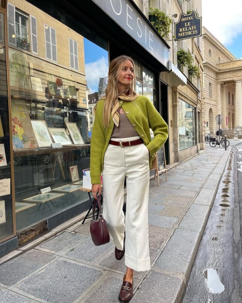 Woman wearing a silk neck scarf with a green cardigan, white wide-leg trousers and burgundy loafers