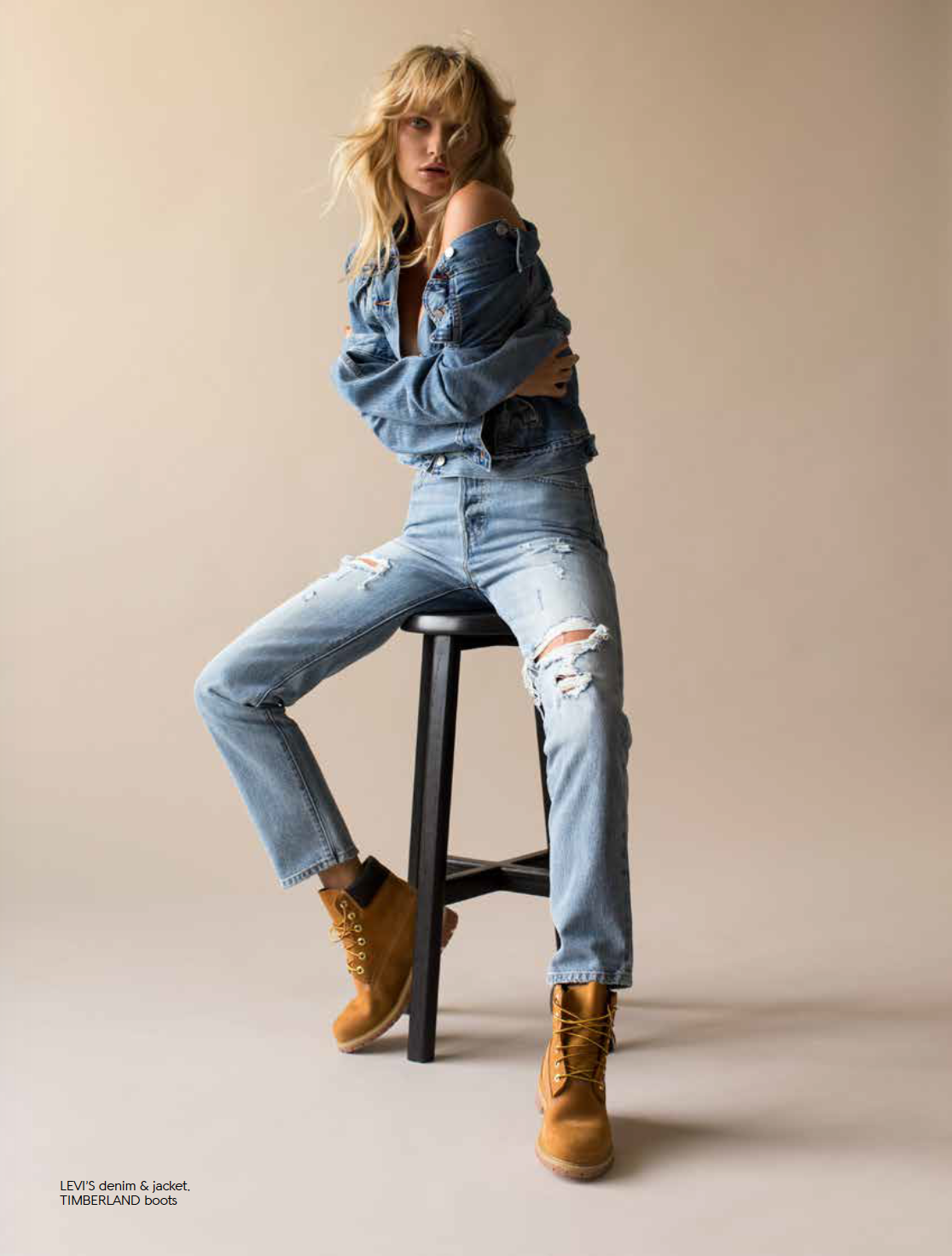 Woman in an off-shoulder denim jacket, light-wash ripped jeans, and wheat Timberland boots