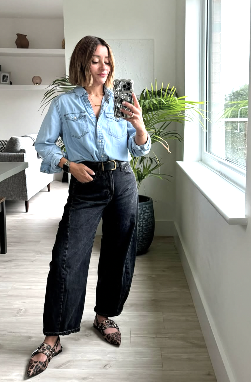 Light blue chambray shirt tucked into dark-wash barrel-leg jeans with black belt and leopard print flats