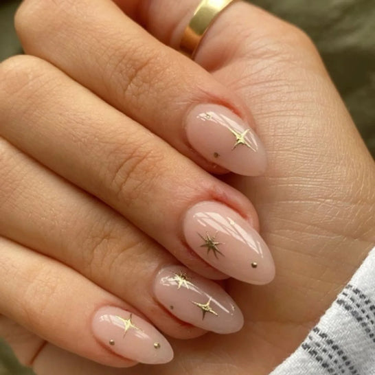 Short nude almond nails with gold starburst art and tiny gold dots