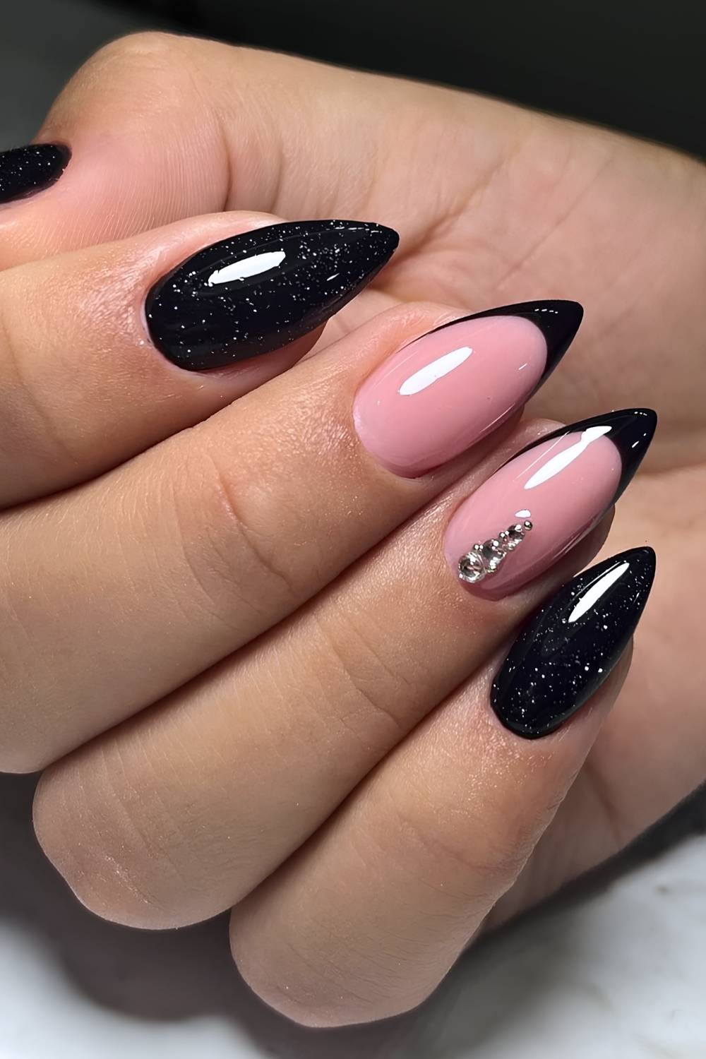 Almond nails alternating black glitter full-cover nails with nude pink nails with black French tips and crystal accents