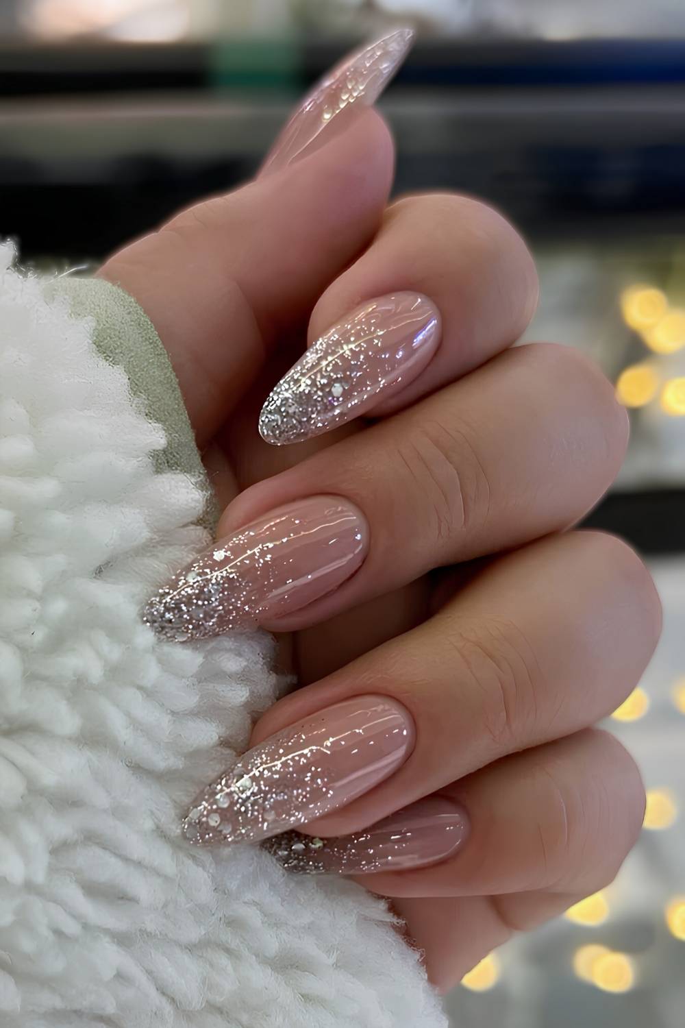 Long almond nails in sheer nude with silver glitter concentrated in a gradient toward the tips