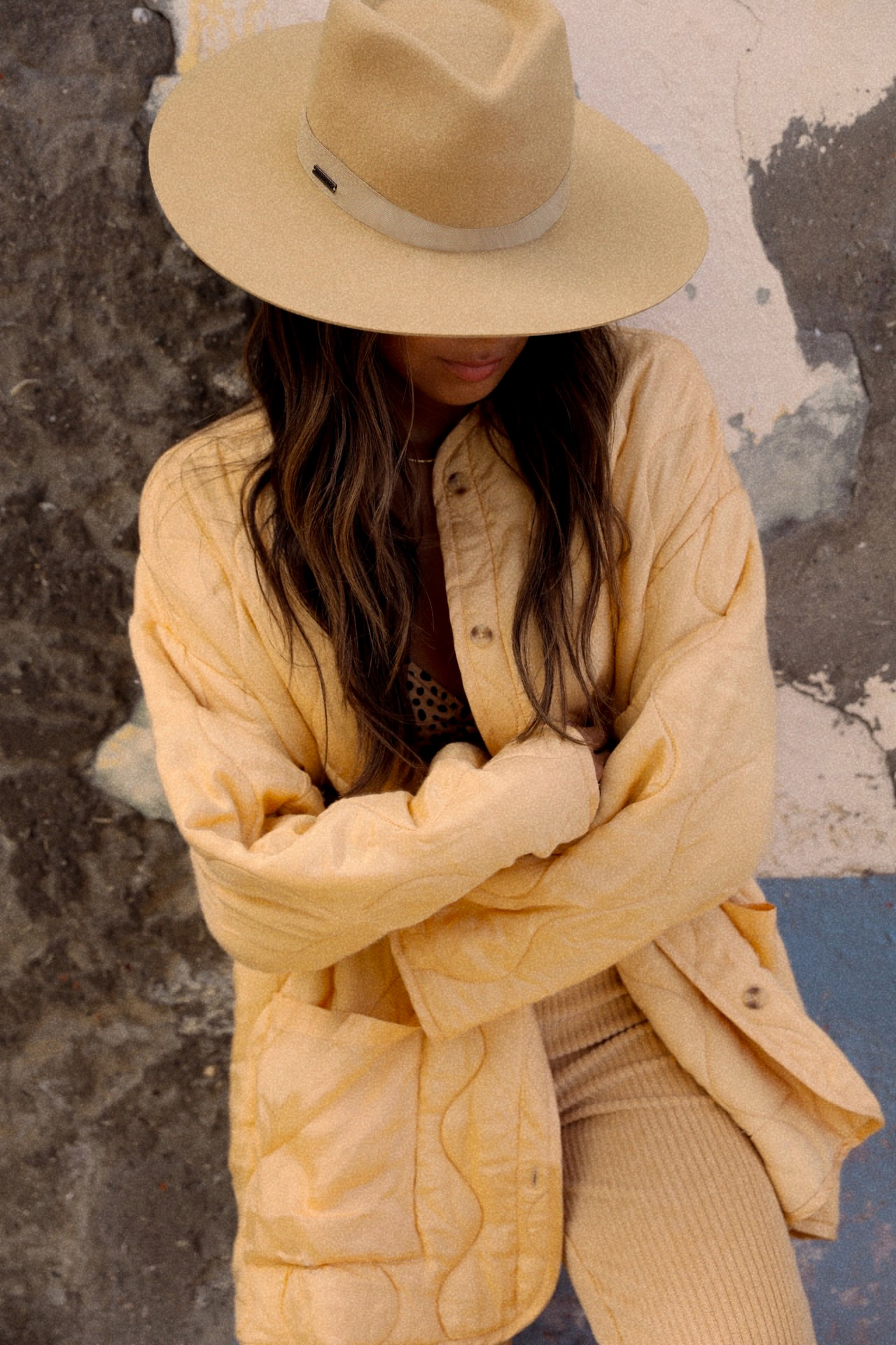 Woman in a yellow quilted jacket with ribbed knit leggings and a wide-brim tan hat