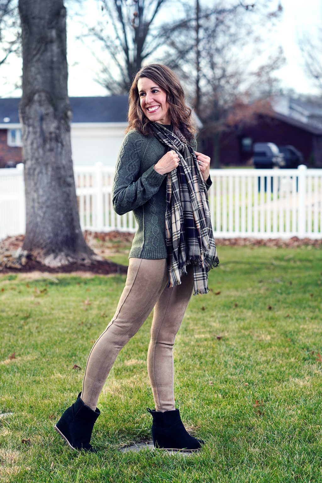 Woman wearing an olive cable-knit sweater with faux-suede leggings, a plaid scarf and ankle boots