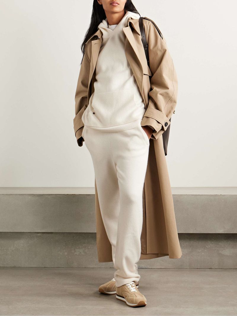 Woman wearing a cream trench coat over a beige hoodie with white sneakers