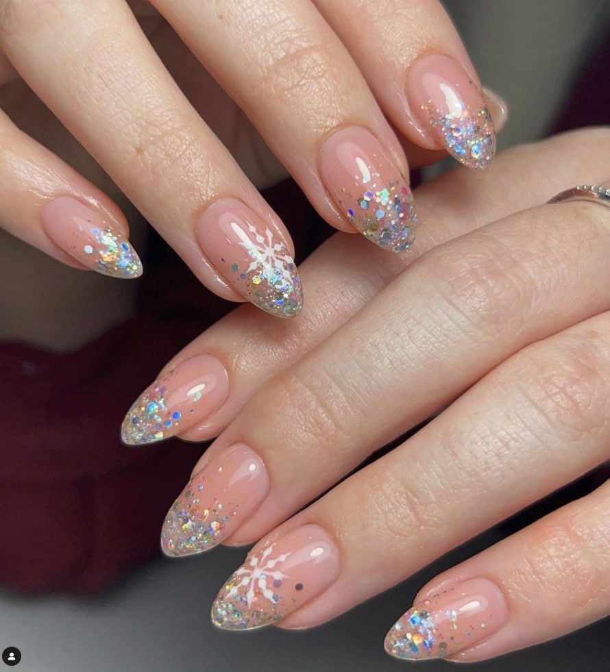 Almond nails on sheer nude with champagne holographic glitter fading to the tips and a snowflake accent