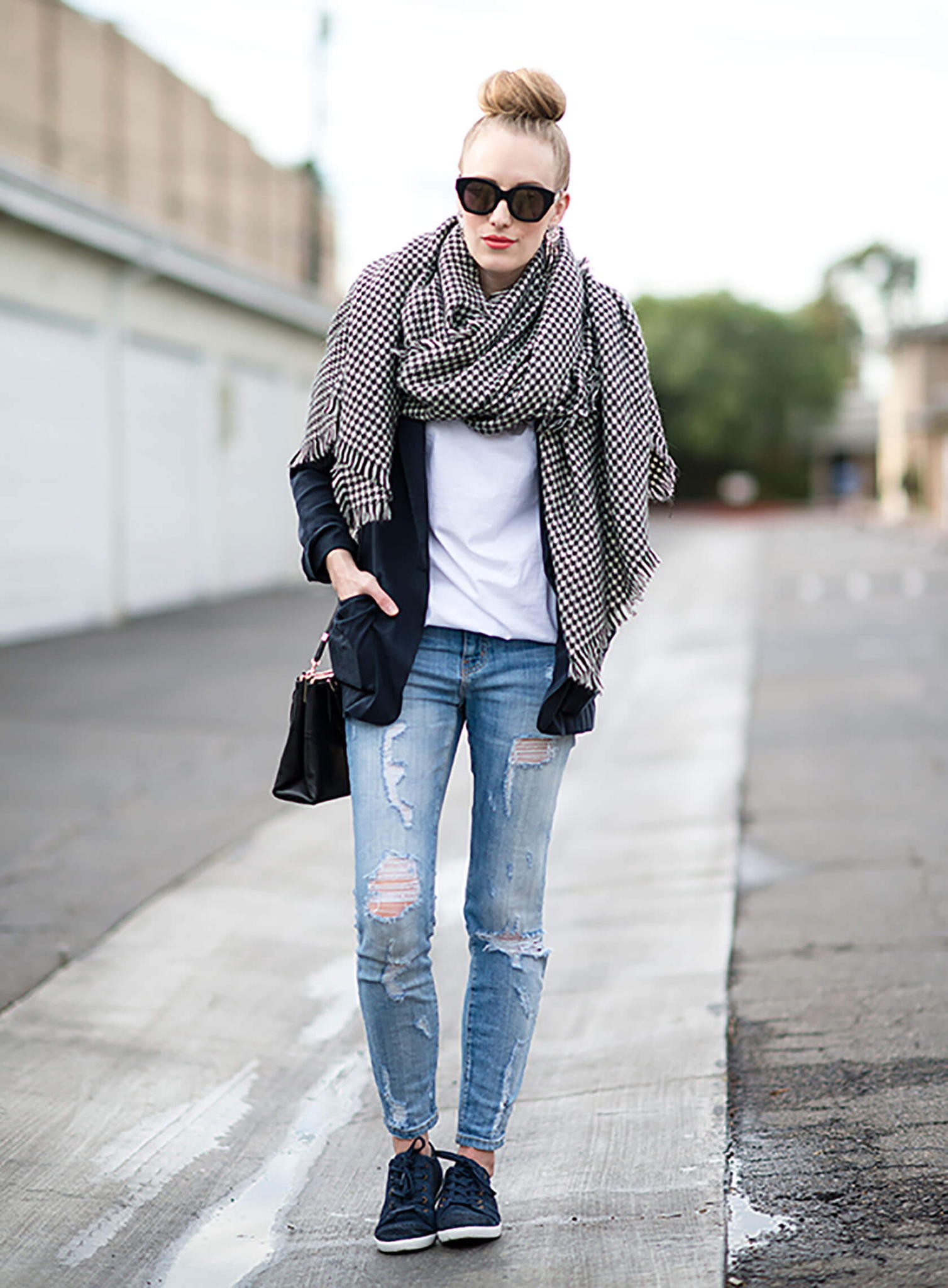 Woman in a black and white houndstooth blanket scarf, navy blazer, white tee and ripped jeans