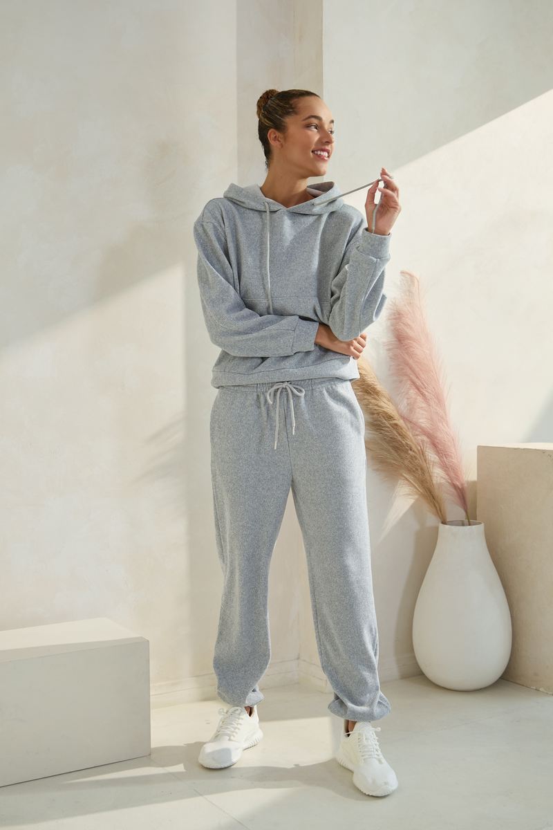 Woman wearing a light grey hoodie and matching jogger sweatpants with white sneakers in a bright studio