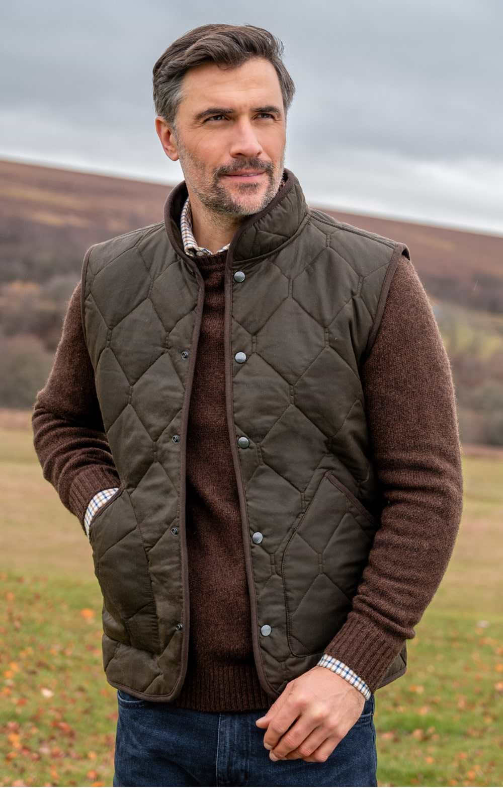 Man wearing an olive quilted gilet vest over a brown knit sweater outdoors