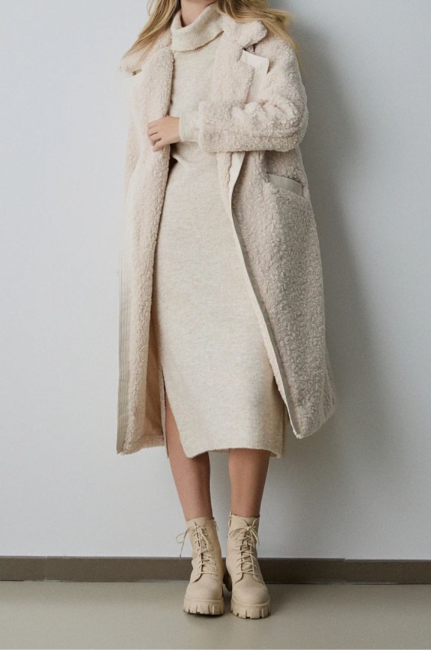 Woman in an ivory teddy coat over a cream knit midi dress with cream lace-up boots