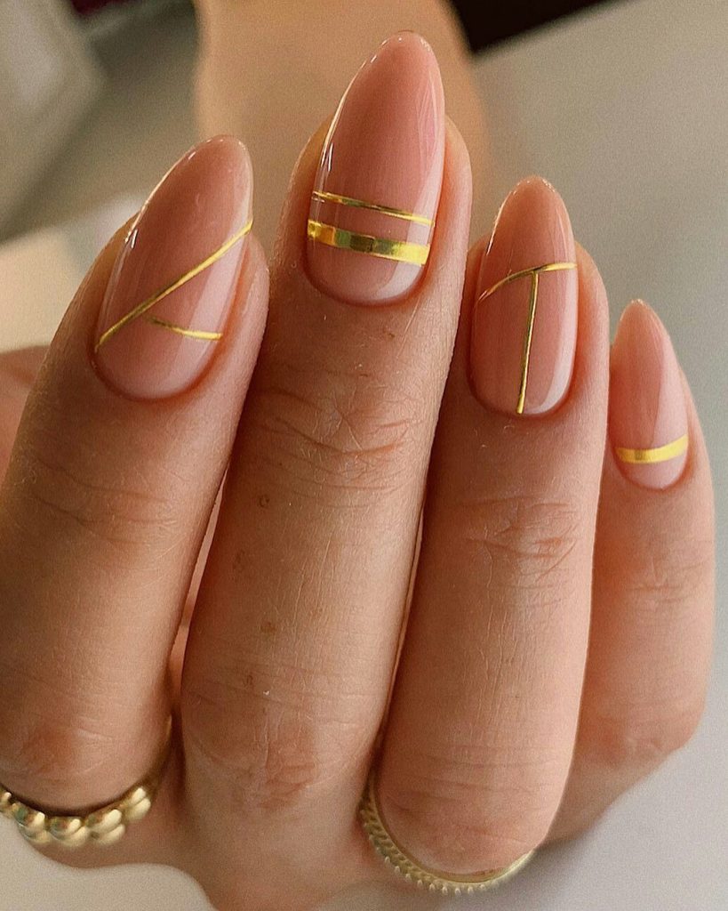 Almond nails with nude polish and thin gold striping tape lines in geometric patterns