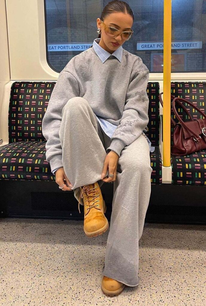 Woman in an oversized grey sweatshirt and sweatpants with a light blue collared shirt underneath and tan Timberland boots