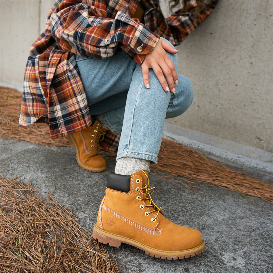 Woman in a rust plaid flannel shacket, light-wash jeans, grey socks, and wheat Timberland boots