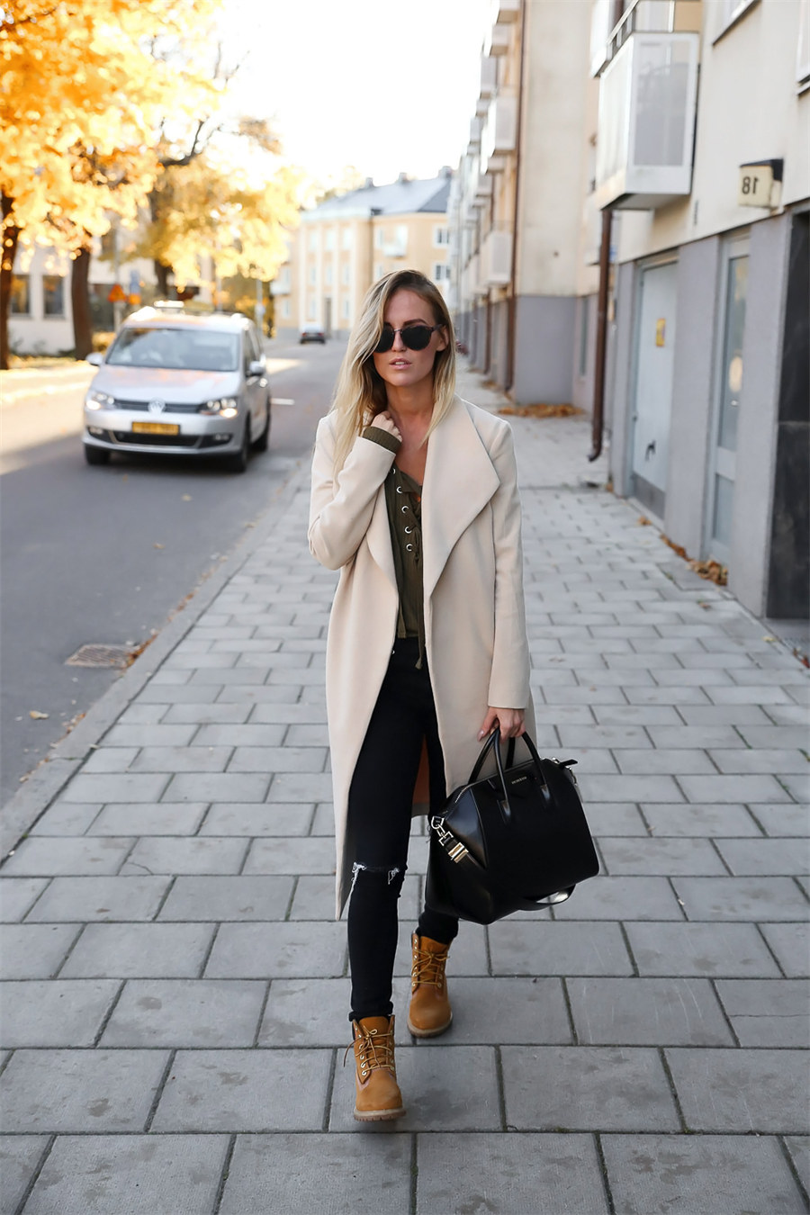Woman in a cream wrap coat, olive lace-up top, black ripped skinny jeans, and wheat Timberland boots