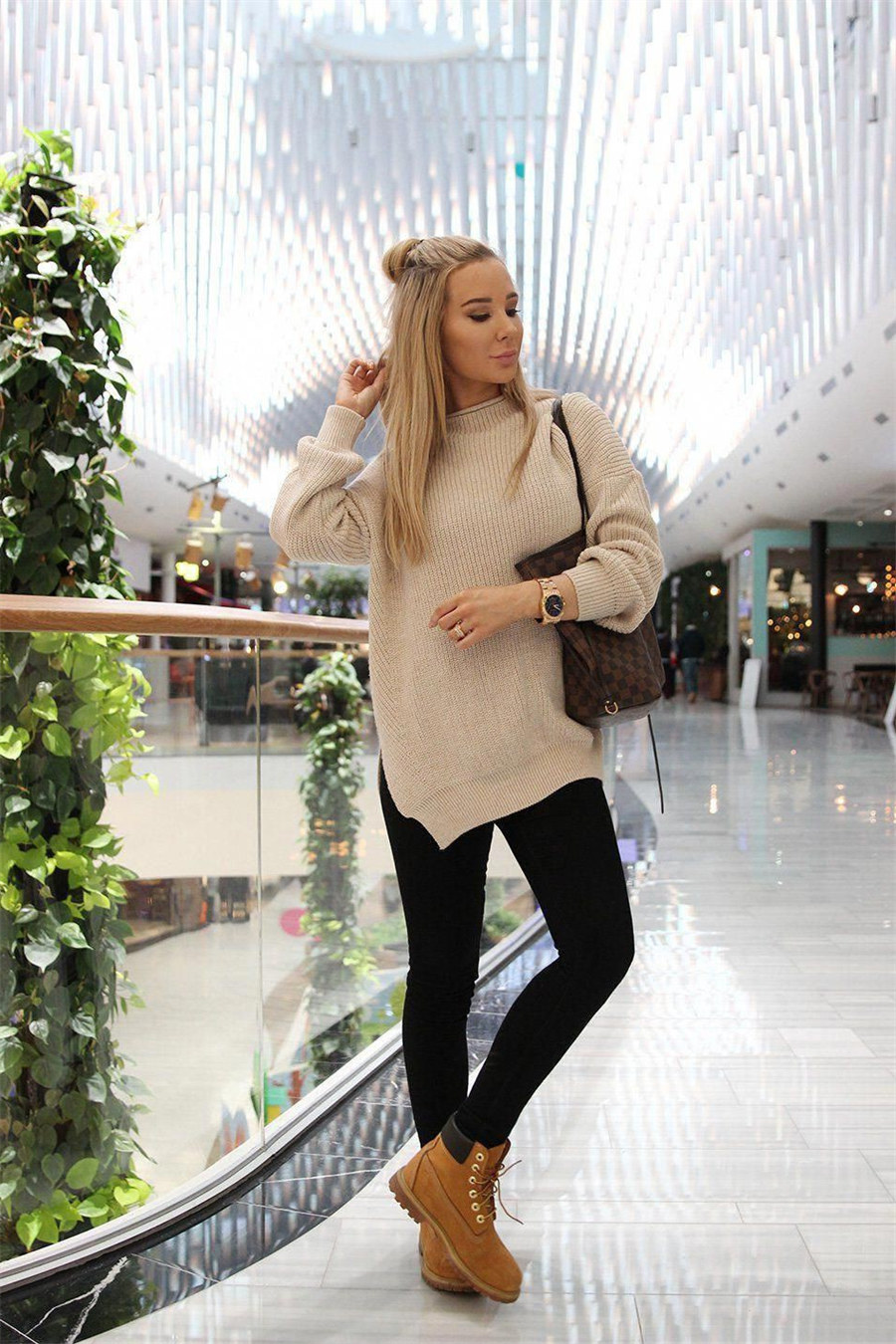 Woman in an oversized beige turtleneck sweater, black leggings, and wheat Timberland boots