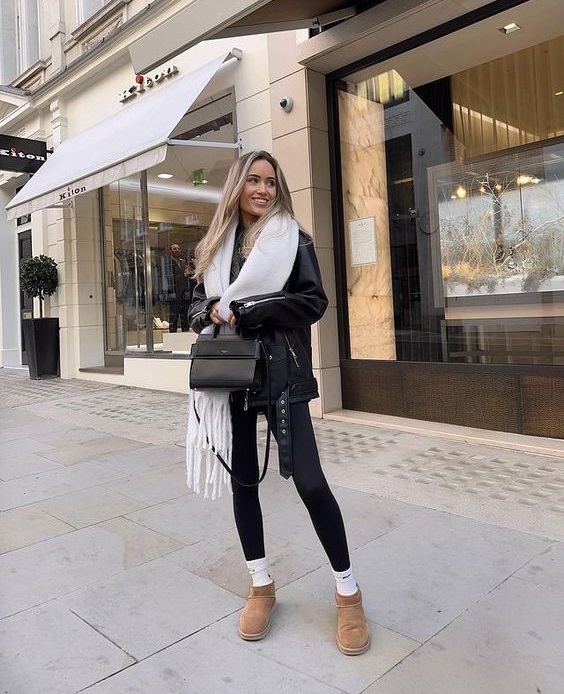 Woman in a black leather jacket and leggings wearing chestnut mini ugg boots with white socks