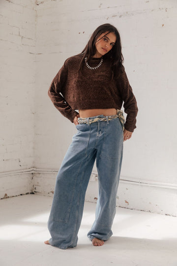 Woman in a brown cropped knit sweater and light-wash low-rise wide-leg jeans with a chunky necklace
