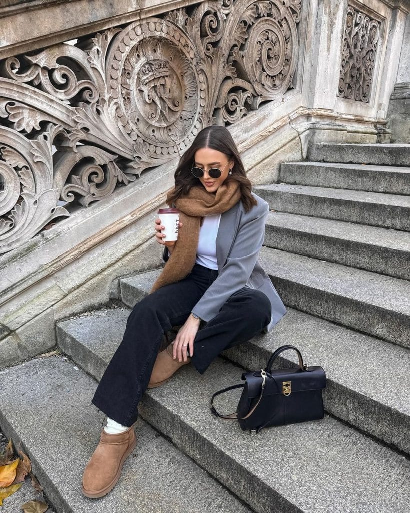 Woman in a grey blazer and black wide-leg jeans wearing chestnut mini ugg boots with a tan scarf