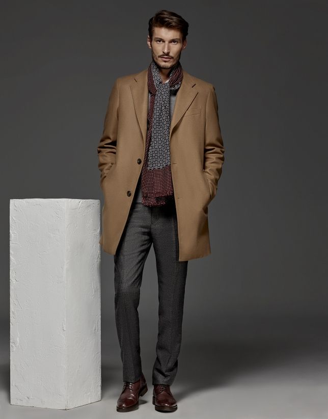 Man in a camel coat with a burgundy patterned scarf, grey trousers and burgundy shoes