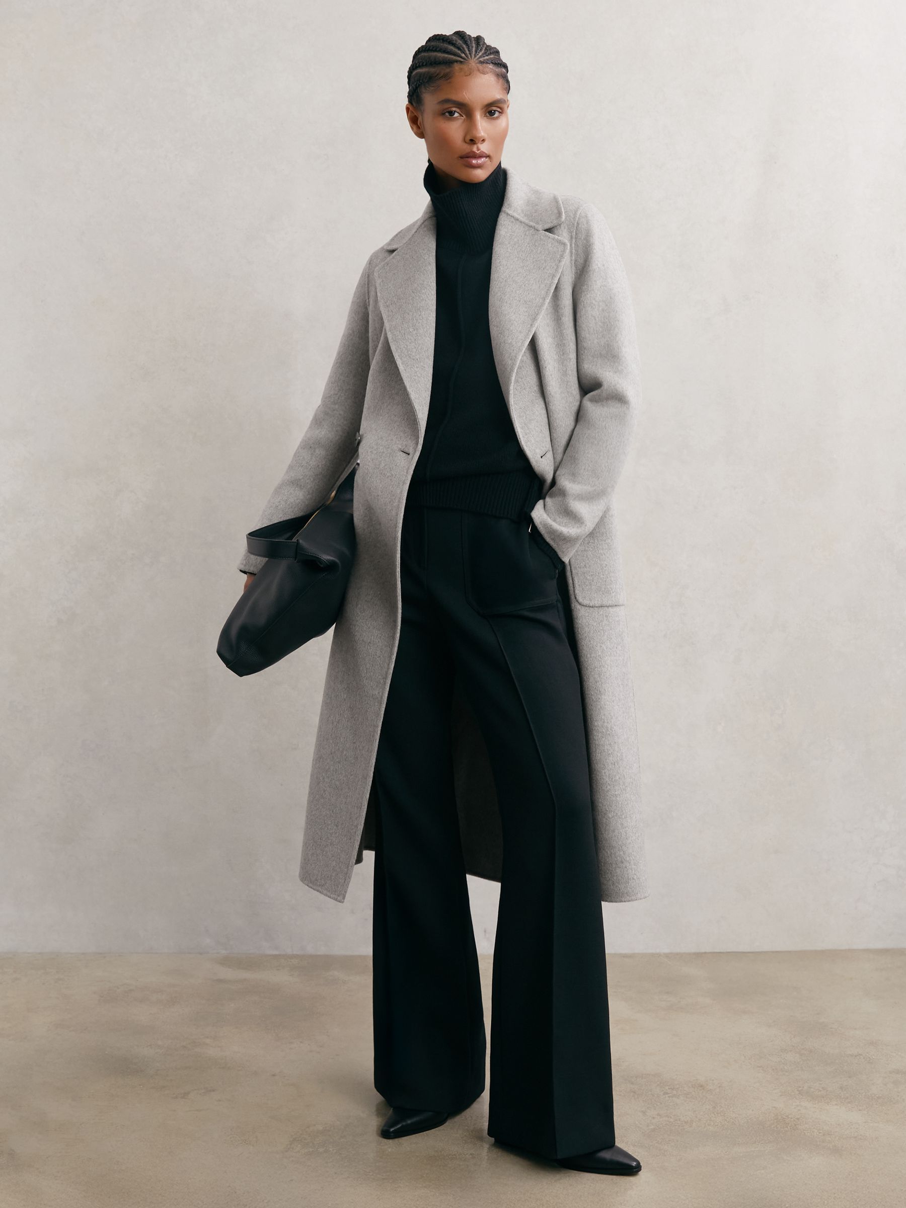 Woman in a light grey long wool coat over a black turtleneck and black wide-leg trousers